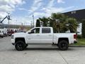 A white 2017 Chevrolet Silverado 1500 with a crew cab and lifted suspension parked beside some palm trees