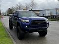 A blue 2022 Toyota Tacoma with a black grille and large off-road tires parked on the side of a street