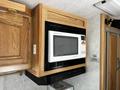 A white Sharp microwave mounted above a black vent in a wooden cabinet inside a 2000 Ford Motorhome