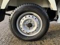 A close-up view of a 2008 Suzuki Carry's wheel with a black tire and silver rim featuring a circular design and visible brand markings