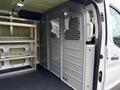 Interior of a 2023 Ford Transit showing a partition wall with ventilation holes and metal shelving on one side
