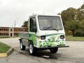 A 2019 CanEV Might-E, a small electric utility vehicle, featuring a green leaf design and a compact body with a flatbed for transporting goods