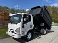 A white 2016 Isuzu NPR dump truck with its bed raised is parked, showcasing its cab and chassis configuration