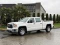 White 2015 GMC Sierra 1500 pickup truck with chrome accents and a bed liner parked on a wet surface