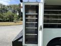 A side view of a 2009 GMC C5500 with an open compartment revealing several metal shelves designed for storage