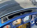 Close-up of a blue motorcycle dashboard featuring round gauges for speed and fuel, with a compartment above for storage