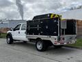 A 2007 Ford F-550 truck with a white cab and a black utility box on the back featuring multiple storage compartments and a high-visibility light bar