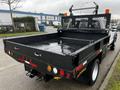 A 2015 Ford F-550 truck with a black flatbed featuring a metal mesh back and various lights and reflectors on the rear