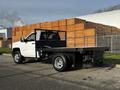 A 2017 Chevrolet Silverado 3500HD with a flatbed and a black mesh guard on the back parked alongside a stack of wooden pallets