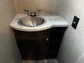A compact bathroom sink with a silver bowl set into a curved marble countertop alongside a dark wood cabinet featuring a door and open shelving