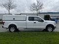 A white 2017 Ford F-150 truck with a cap on the bed is parked with a side view showing four doors and five-spoke alloy wheels