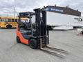 A 2011 Toyota Forklift with an orange and black color scheme featuring two metal forks in the front and a driver's seat visible in the cabin