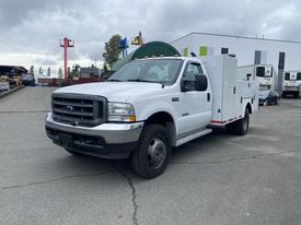 A white 2003 Ford F-450 Super Duty truck with a utility body and side compartments is parked, showcasing its robust design and heavy-duty build