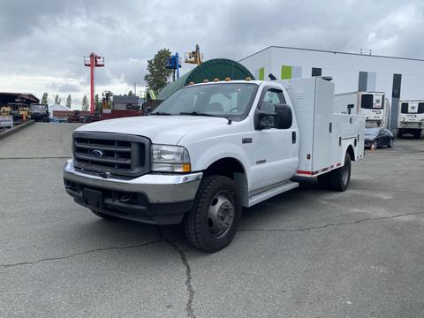A white 2003 Ford F-450 Super Duty truck with a utility body and side compartments is parked, showcasing its robust design and heavy-duty build