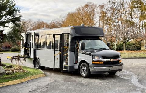 A 2019 Chevrolet Express shuttle bus with a black and silver exterior featuring an accessible ramp on the side and large windows