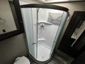 A spacious shower enclosure with a curved glass door featuring a showerhead and a wall-mounted faucet inside a recreational vehicle bathroom