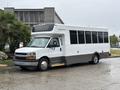 A 2020 Chevrolet Express passenger bus with a white exterior and large tinted windows parked on a wet surface