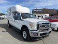 A white 2014 Ford F-350 Super Duty with a camper shell on the bed and chrome accents on the front grille and bumper