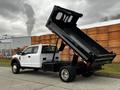 A white 2019 Ford F-550 dump truck with its bed raised in a dumping position