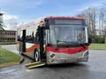 A red and silver 2016 Grande West Vicinity bus with a ramp deployed for accessibility parked on a curb