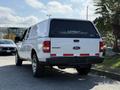 A white 2009 Ford Ranger pickup truck with a camper shell is parked, showcasing its rear view with a black and white logo on the shell and red accent stripes on the tailgate