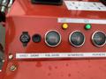 A control panel featuring a 12-volt outlet a choke switch a fuel gauge an oil temperature gauge and an hour meter with indicators in a red casing