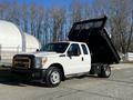 A 2011 Ford F-350 SD in white with a black dump bed raised at the back and orange lights on the roof