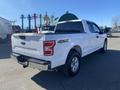 A 2019 Ford F-150 in white with a truck bed and chrome accents viewed from the rear angle showing its 4x4 badge and alloy wheels