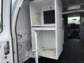An open white shelving unit inside a Ford Econoline van with a lower cabinet and an upper compartment showing signs of wear