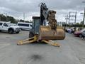 A 2012 John Deere 310SJ backhoe loader facing forward with a large front bucket and stabilizer legs extended on either side
