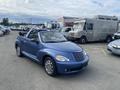 A blue 2007 Chrysler PT Cruiser convertible with a black interior and a soft top, parked with its top down, showcasing its distinctive rounded design and chrome wheels