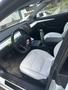 Interior of a 2022 Tesla Model 3 featuring white leather seats a large touchscreen display and a modern minimalist design with a center console and cup holder