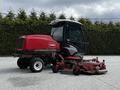 A red 2012 Toro Groundsmaster lawn mower with a cab and a rear-mounted mower deck positioned for maintenance or storage