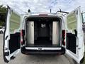 A 2023 Ford Transit van with its rear doors wide open showcasing a spacious, empty cargo area with metal shelving on both sides