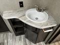 A countertop with a round sink and dual metal faucets in a recreational vehicle bathroom featuring a curved design and storage compartments below