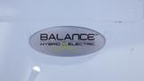 A silver emblem that reads "BALANCE HYBRID ELECTRIC" with a stylized logo on a white surface