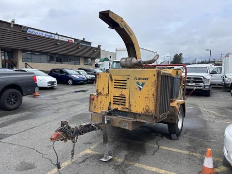 A yellow 2015 Vermeer Corporation BC1200XL wood chipper with a chute on top and a wheeled trailer hitch in the back