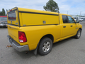A yellow 2015 RAM 1500 pickup truck with a matching cap on the truck bed parked on an asphalt surface