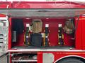 A red fire truck with an open compartment displaying four seats mounted on yellow frames and covered in black and tan fabric
