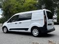 A 2016 Ford Transit Connect van in white with black accents parked on a gravel surface with a side view showcasing its sliding door and alloy wheels