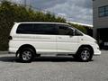 A 2003 Mitsubishi 7 Passenger Van in white with chrome wheels and side graphics parked on a surface with gravel