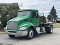 A green 2013 Kenworth T370 heavy-duty truck with a flatbed and chrome accents parked on a street