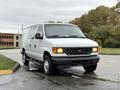 A 2006 Ford Econoline van in white, featuring sliding side doors, a front grille with the Ford logo, and standard headlights positioned on either side of the grille