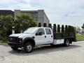 A 2008 Ford F-550 truck with a flatbed carrying several tall evergreen shrubs