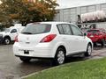 A white 2012 Nissan Versa parked with a hatchback design and rear hatch door raised