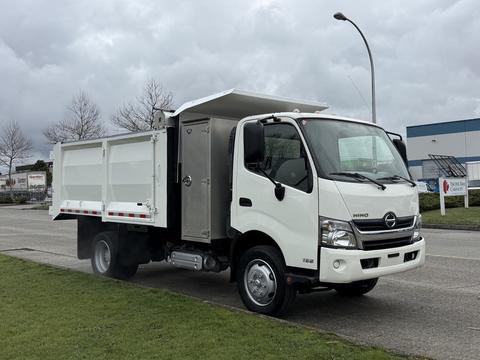 A 2014 Hino 195 truck with a white exterior and a drop-side bed is parked with its rear compartment open