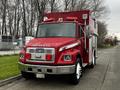 A red 1995 Freightliner FL70 fire rescue truck with a large box-like structure on the rear and visible lights and sirens on top