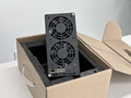 A black mining rig with two fans and various ports is placed inside a cardboard box with foam padding