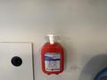 A red hand sanitizer dispenser mounted on a wall with instructions for use and a pump on top