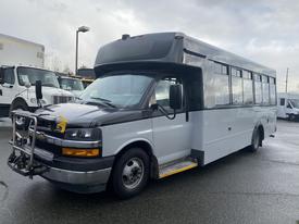 A 2018 Chevrolet Express bus with a mostly white exterior and a black front; features a front-mounted push bumper and step entrance at the side